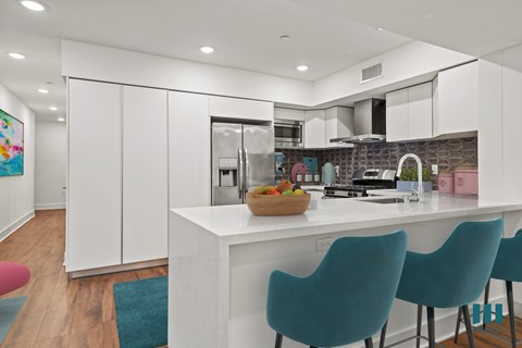 A kitchen with white cabinets and a white island with blue chairs.